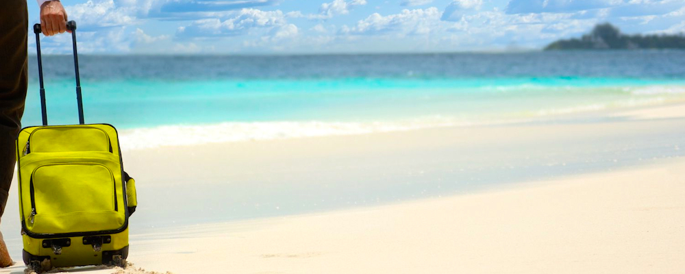 Businessman with suitcase walking on the beach towards sea planning to travel to Aruba