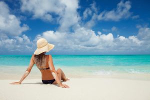 a girl wearing a hat and getting a tan on a tropical beach