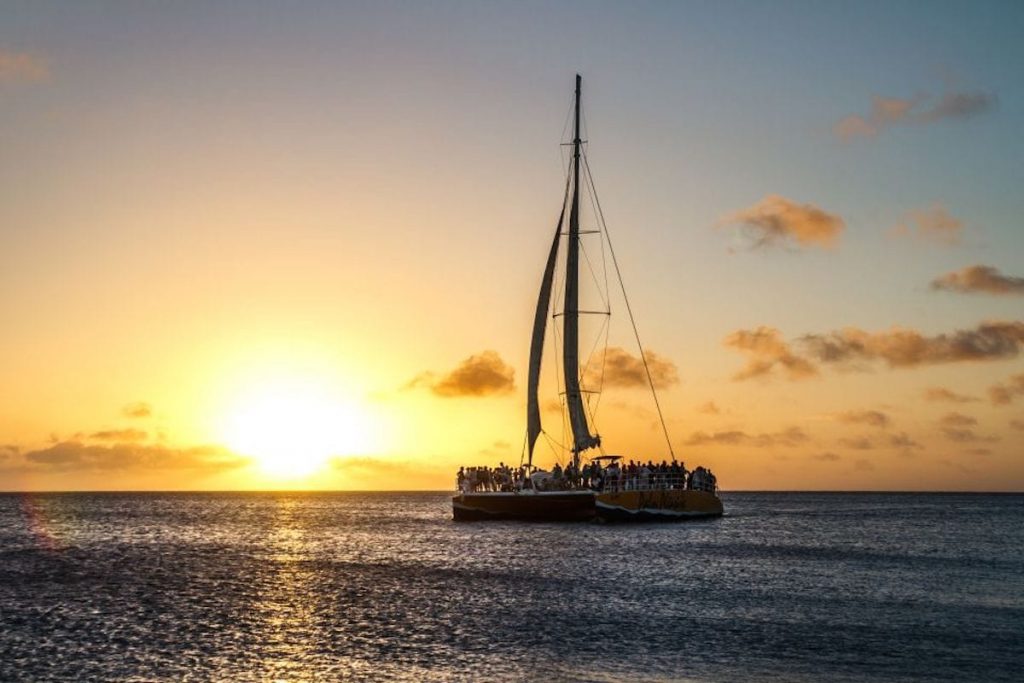 A large group of people on a catamaran, sailing into the Aruban sunset.