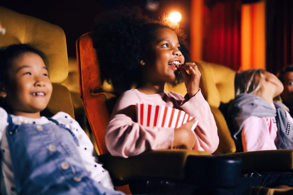 A little girl sits comfortably in a movie theater seat, wholly engrossed in the cinematic experience.
