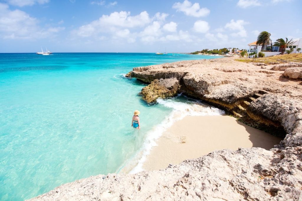 In the picture of Tres Trapi in Aruba, you are greeted by a captivating scene that showcases the allure of this snorkeling spot. The image captures a stretch of pristine sandy beach with turquoise waters gently lapping against the shore. The beach is embraced by rugged cliffs on one side, adding a touch of natural grandeur to the scenery.